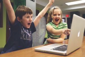 Zwei Kinder am Laptop, die sich beide sehr über ihren Erfolg von Bildung freuen.